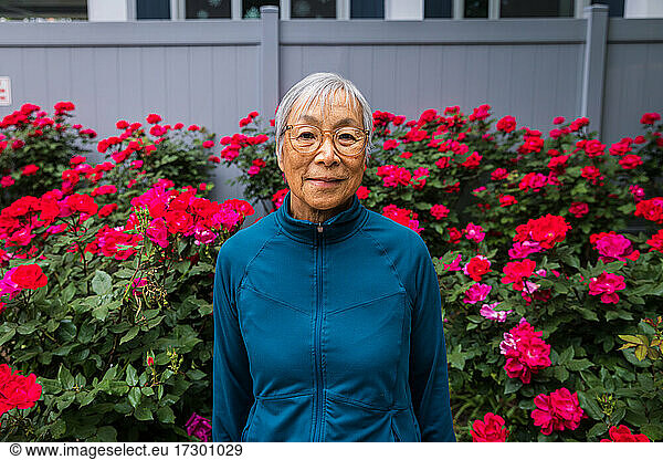 Senior woman wearing eyeglasses standing in front of red flower garden