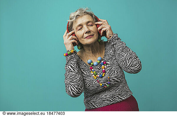 Senior woman wearing headphones listening to music against colored background