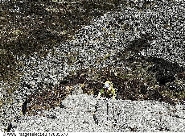 Senior woman wearing helmet climbing rocky cliff on sunny day