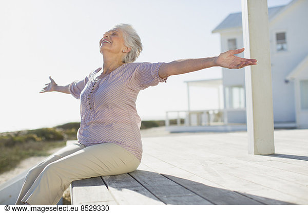Senior woman with arms outstretched on sunny deck