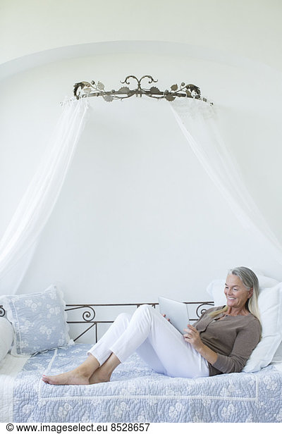 Senior woman with digital tablet relaxing in daybed