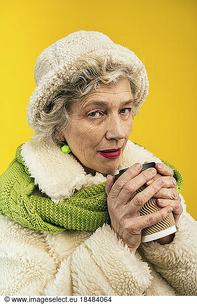Senior woman with disposable coffee cup against colored background