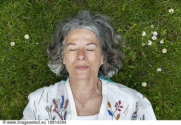 Senior woman with eyes closed lying on green grass