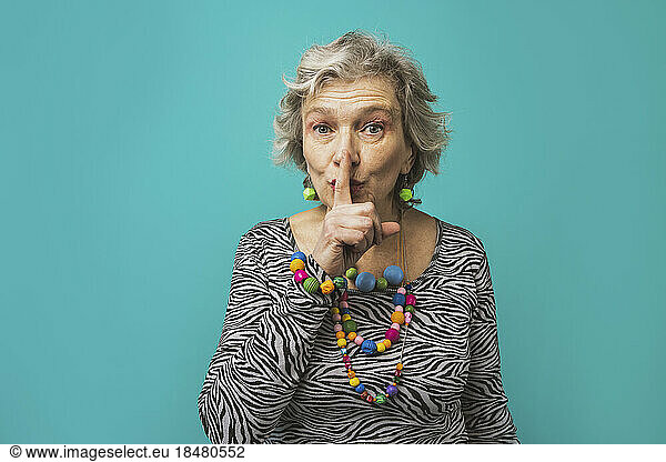 Senior woman with finger on lips standing against colored background