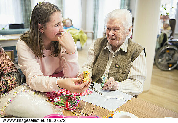 Senior woman with girl holding handmade crochet chick at rest home