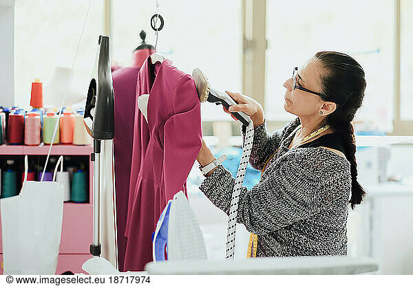 senior woman with glasses ironing a dress in a fashion design studio