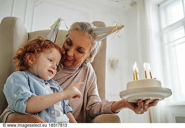Senior woman with grandson holding birthday cake at home