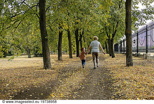Senior woman with grandson holding hands and running in autumn park