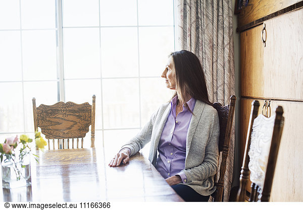 Senior woman with long brown hair sitting at a dining table.