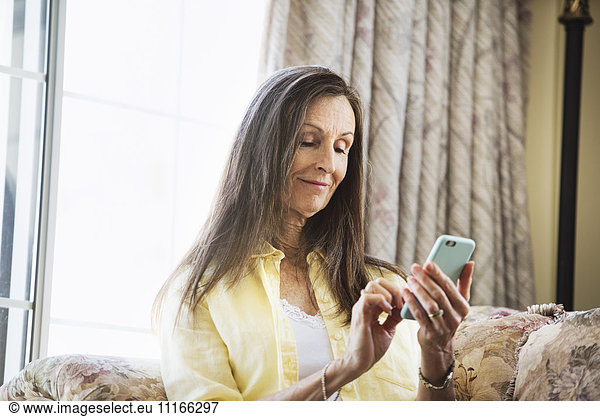 Senior woman with long brown hair sitting on a sofa  using a mobile phone.