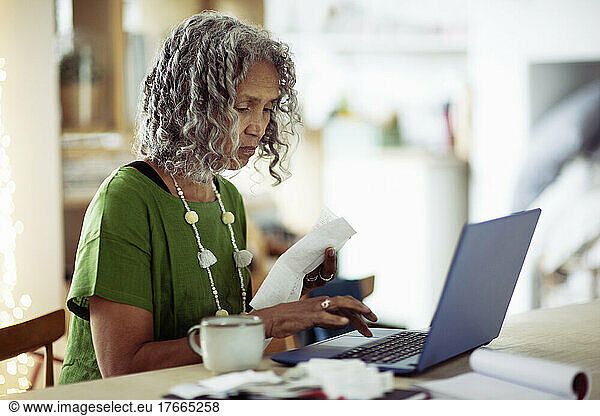 Senior woman with receipts banking at laptop