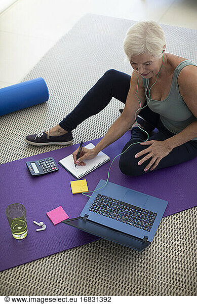Senior woman working at laptop on yoga mat