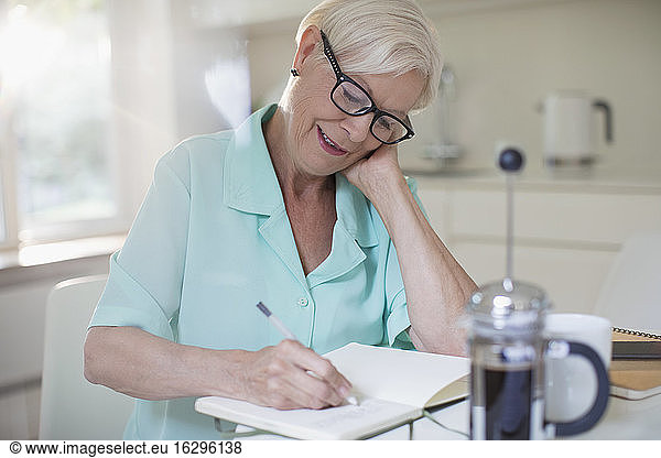 Senior woman writing in journal at morning kitchen
