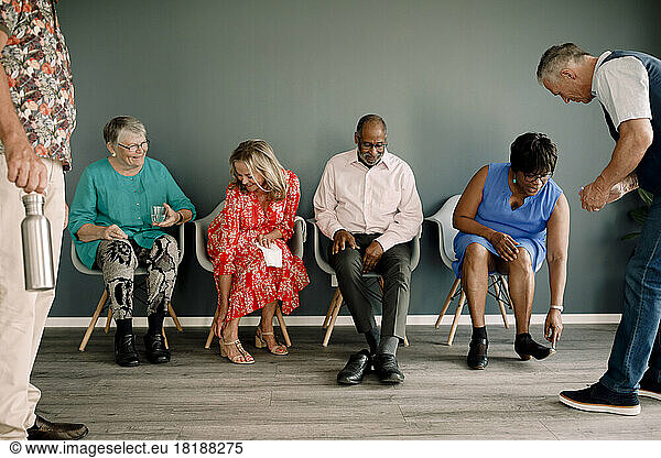 Senior women and men wearing footwear while sitting on chairs by male friends in dance class