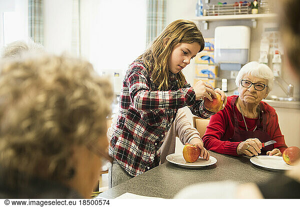 Senior women with girl peeling apple at rest home