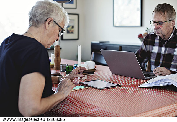 Seniorenpaar  das beim Sitzen am Esstisch Technologien einsetzt.