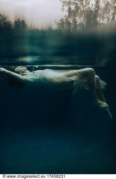 Sensual woman floating underwater facing the sun