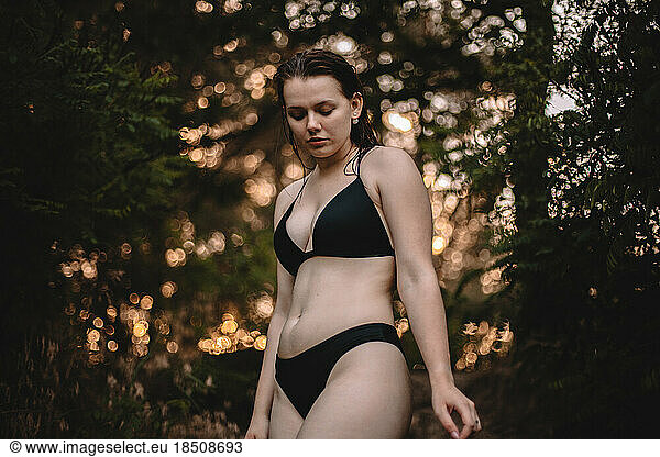 Sensual woman in a bikini standing against trees in forest