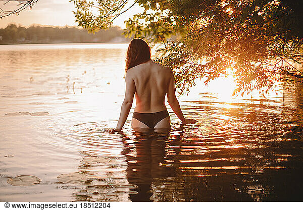 Sensual woman standing in lake under tree at sunset