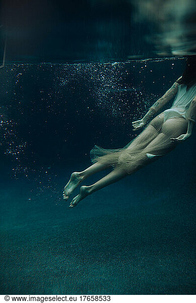 Sensual woman swimming underwater in sheer dress