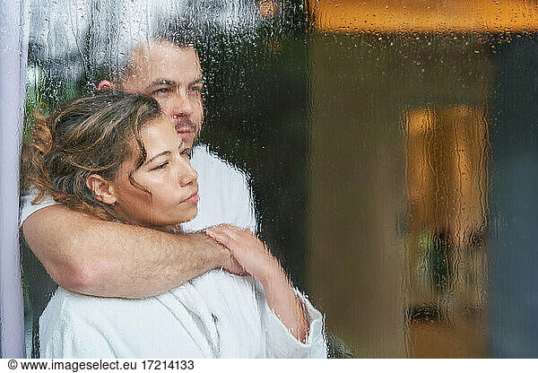 Serene affectionate couple hugging at rainy window
