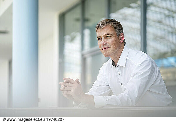 Serene businessman leaning on railing in office building
