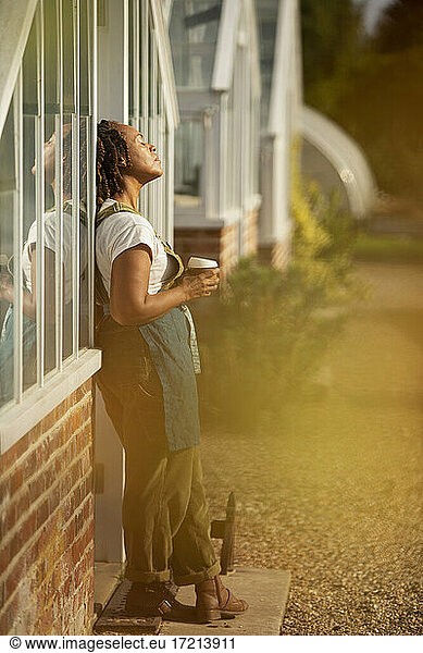 Serene female garden shop owner basking in sunlight with coffee