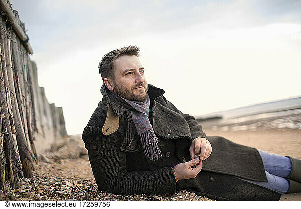 Serene man in winter coat relaxing on beach
