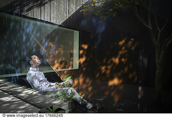 Serene man sitting in sunlight in courtyard