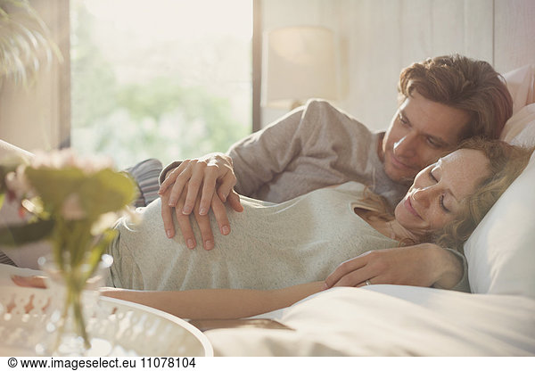 Serene pregnant couple holding stomach on bed