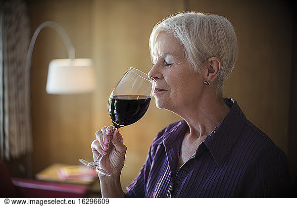 Serene senior woman smelling and tasting red wine