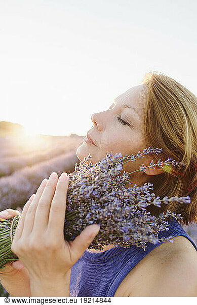 Serene woman holding bunch of lavender flowers in field