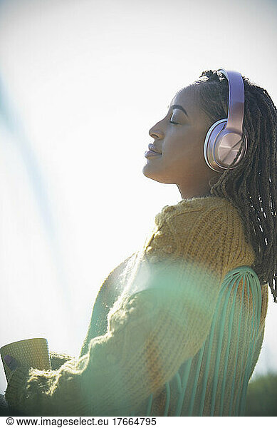 Serene young woman with headphones basking in sunshine