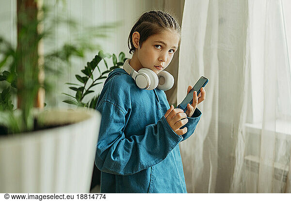 Serious boy with wireless headphones holding smart phone at home