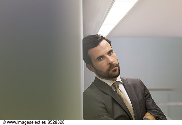 Serious businessman leaning against office wall
