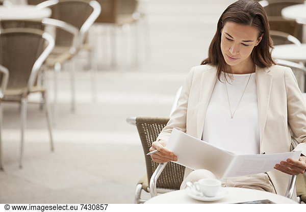 Serious businesswoman reading paperwork at sidewalk cafe