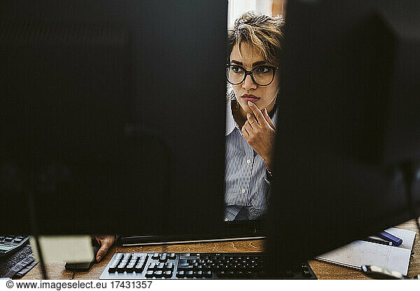 Serious businesswoman seen through computer monitor sitting at desk
