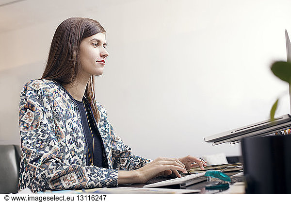Serious businesswoman typing on computer keyboard by wall at office