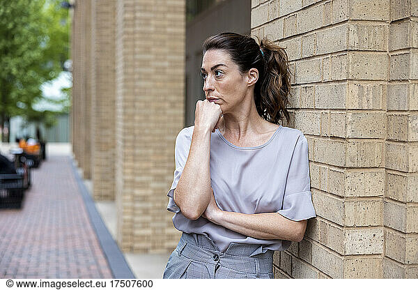 Serious businesswoman with hand on chin by brick wall