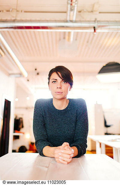 Serious businesswoman with hands clasped leaning on desk in office
