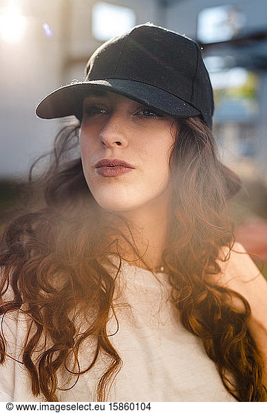 Serious curly woman wearing a cap in the street with lens flare