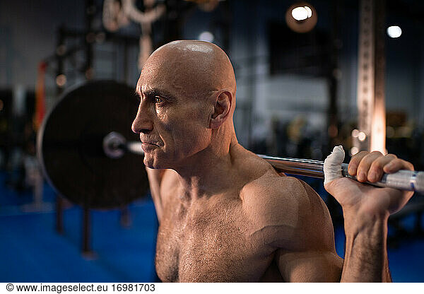 Serious elderly sportsman exercising with barbell