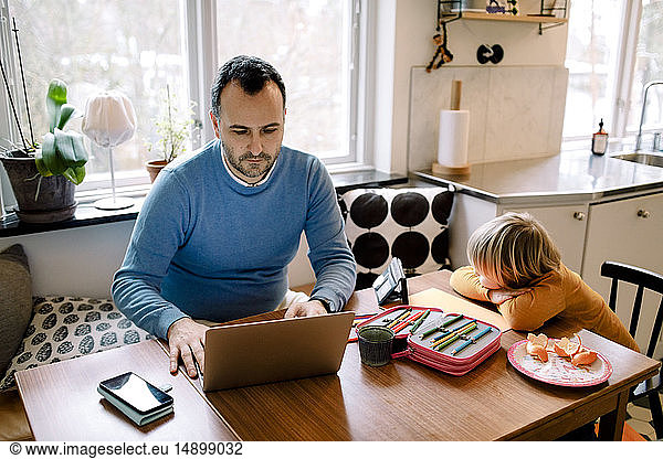 Serious father using laptop while daughter watching mobile phone at home