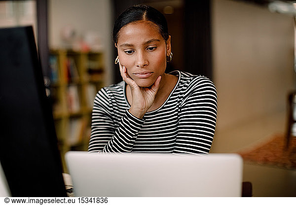 Serious female entrepreneur looking at laptop while sitting in workplace