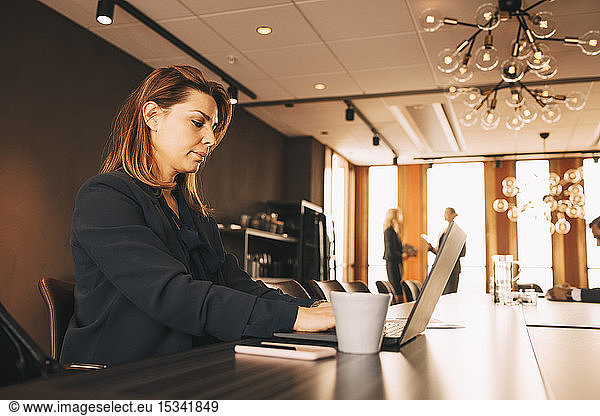 Serious female financial advisor working on laptop at conference table in board room