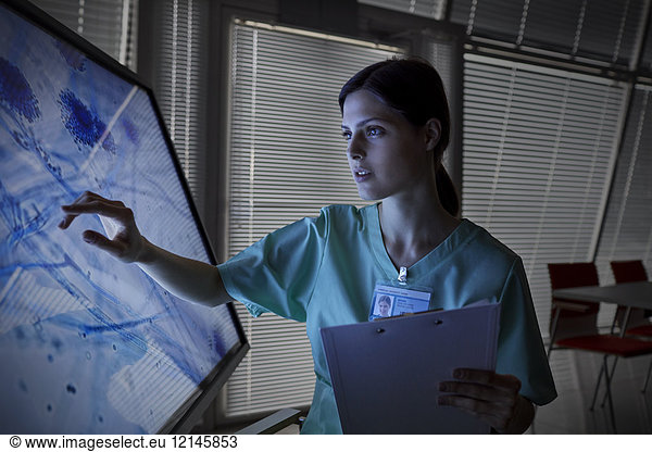 Serious female nurse using touch screen computer monitor  viewing microscope slide