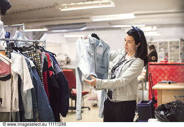Serious female volunteer looking at jacket by clothes rack in workshop