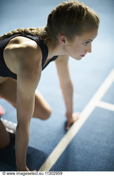 Serious focused female runner ready at starting block on sports track