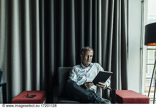 Serious Geschäftsmann mit digitalen Tablette gegen grauen Vorhang im Büro Cafeteria