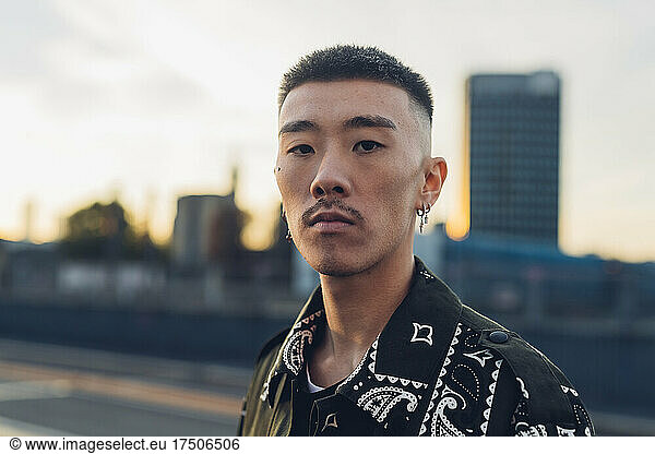 Serious hipster young man in city at sunset